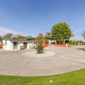 A small building with a courtyard and large tree under a clear sky.