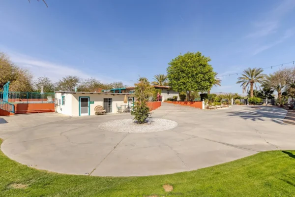 A small building with a courtyard and large tree under a clear sky.