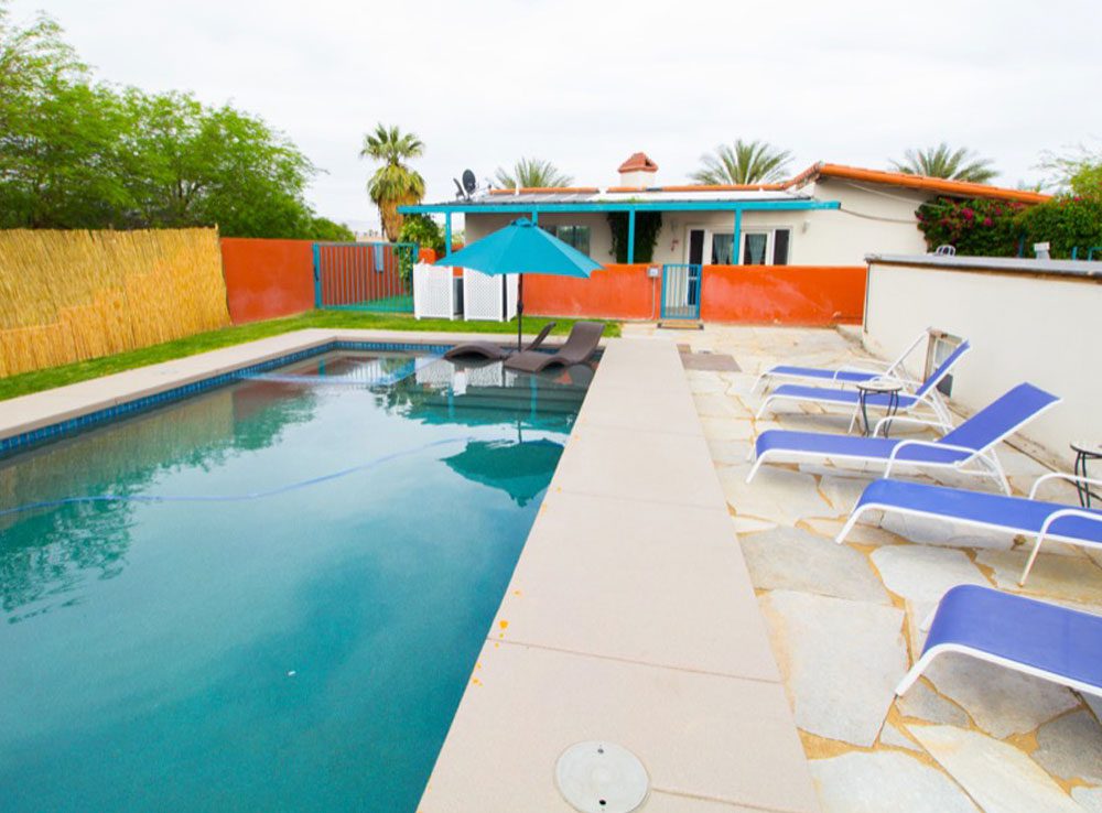 A pool with chairs and umbrellas in the back yard.